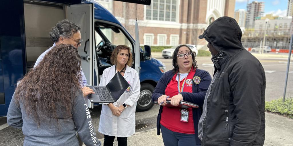 A group of medical providers stand outside and speak to an unhoused Veteran.