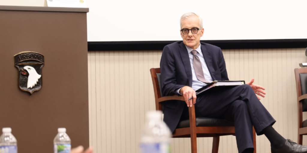 Secretary of VA sits while addressing U.S. soldiers in uniform.