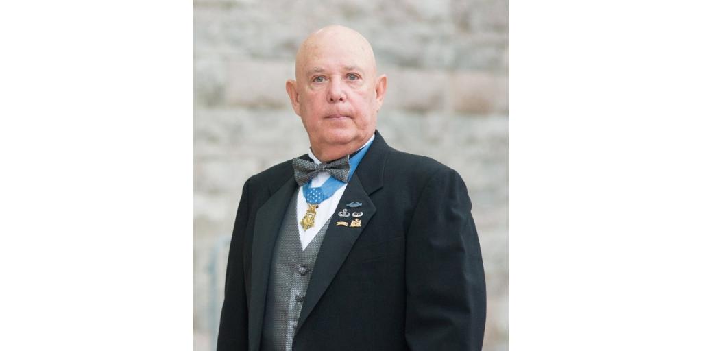 A man in formal dress is poses for his portrait. Around his neck is the Medal of Honor.