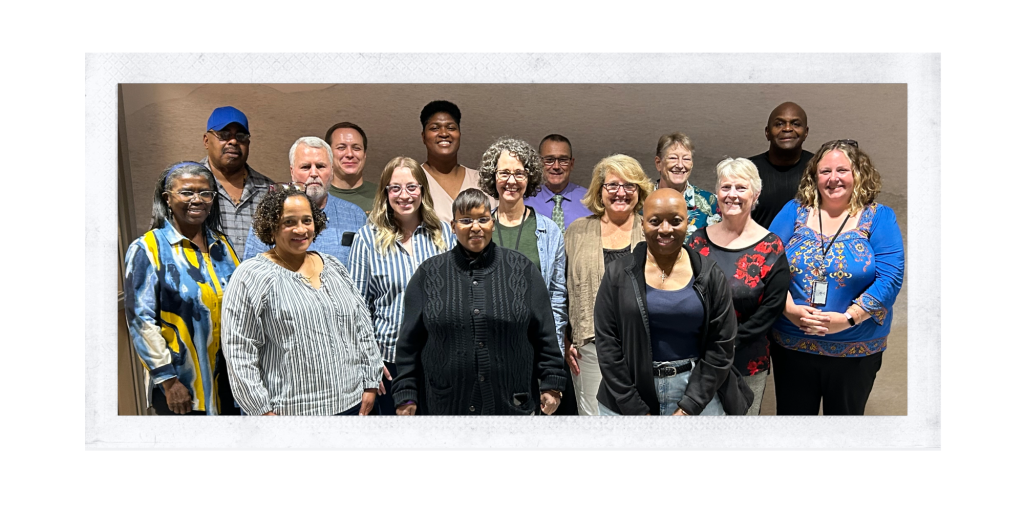 Group of people standing in two rows in front of a gray background.