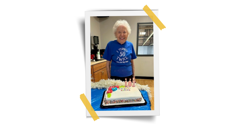 white frame with person with short, white hair standing behind a cake that says "101 happy birthday Marion"