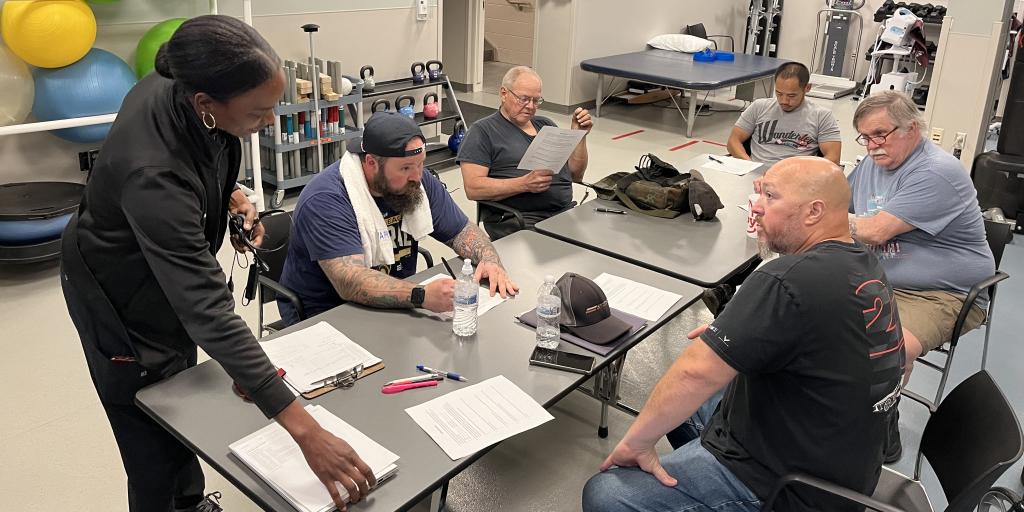 Veterans in the gym environment sit at a table and go over physical therapy and rehabilitation progress reports
