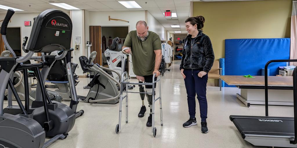 Male Veteran uses a walker while female Physical Therapist assists him.