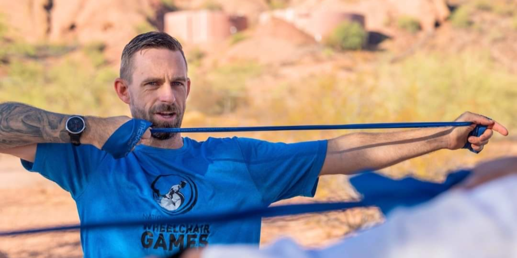 A man in a blue shirt demonstrating how to stretch using an elastic band.