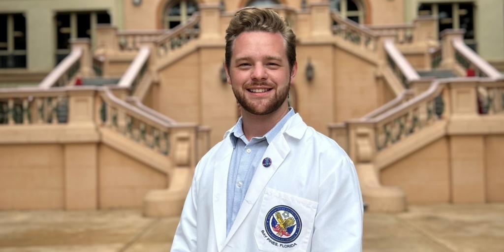 A man stands outside in a white lab coat smiling. 