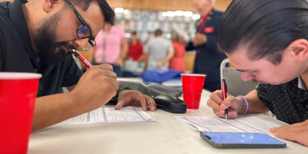 Two men seated at a table filling out paperwork.