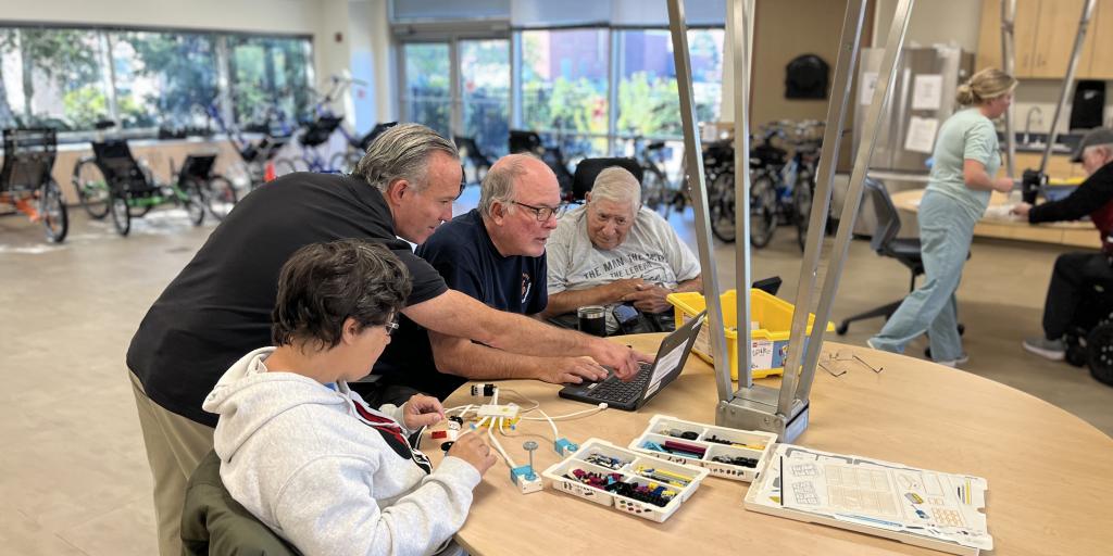 Classroom environment, instructor assisting three people with a lego robot project.