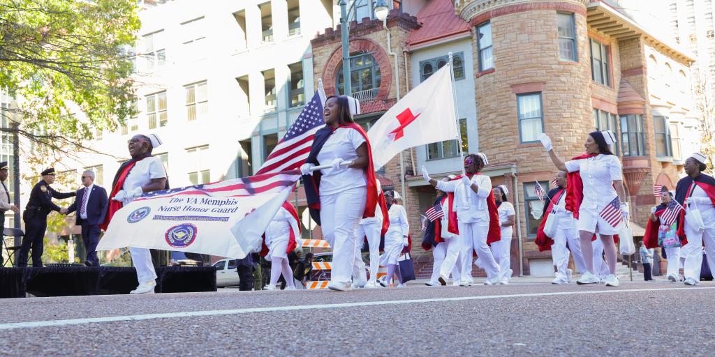 Nurses walking down Memphis city street during Veterans Day parade with flags and banners.