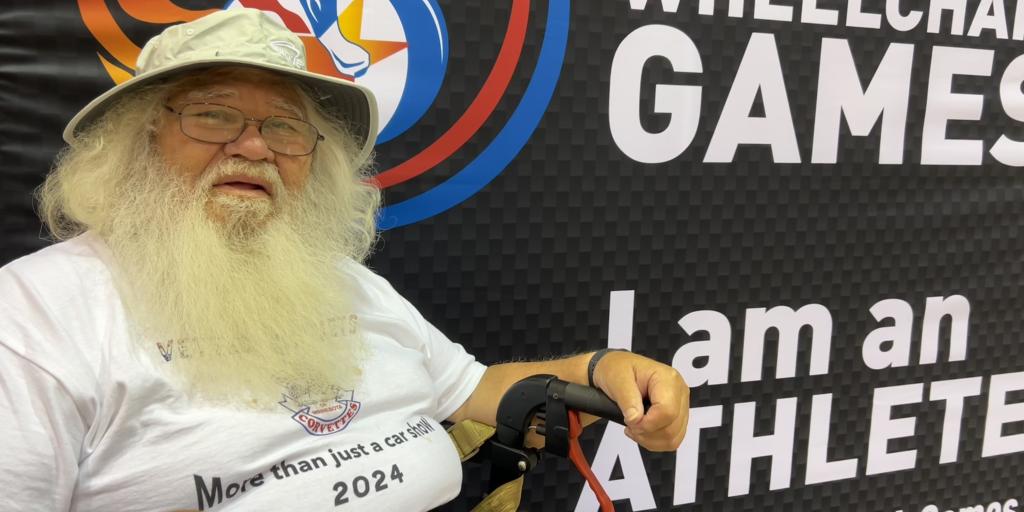 Joe Mauricio sitting in front of a banner for the Wheelchair Games
