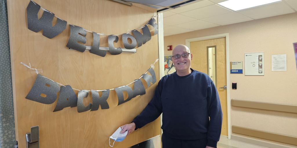 Man standing next to "Welcome Back" sign