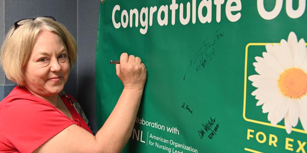 A photograph of Denise Carillo, RN signing the Daisy Award Banner.