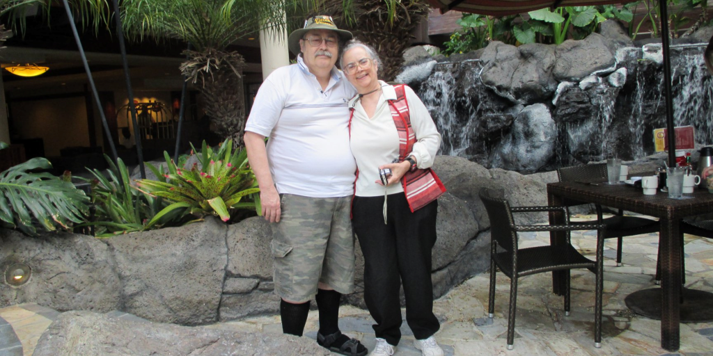 A couple smiling and posing together for a photograph in a scenic outdoor setting.