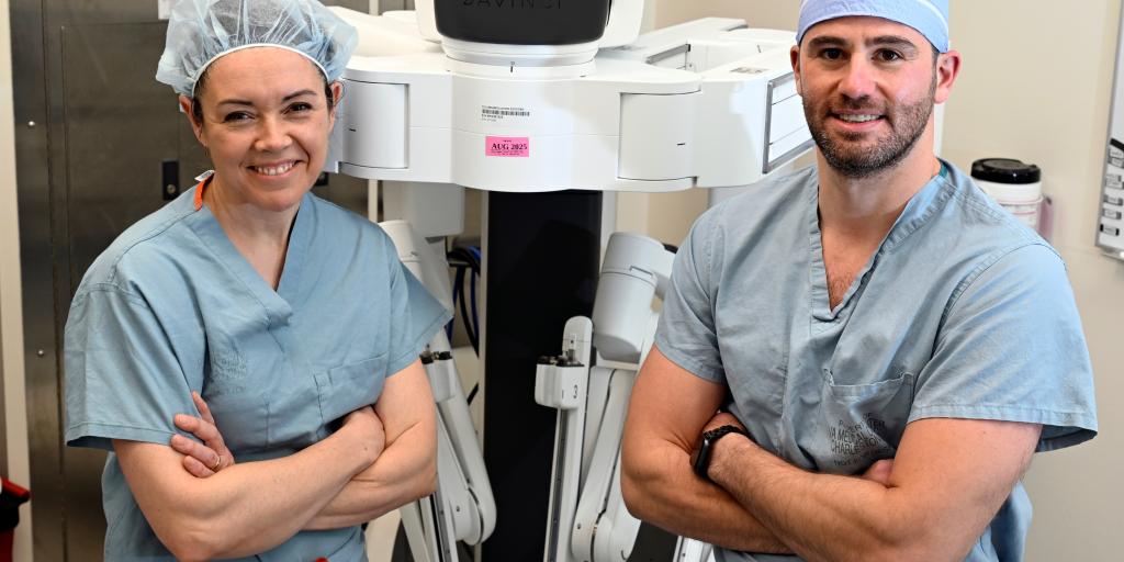 Dr. Evans , left, and Dr. Stone pose for a photo in front of a DaVinci Surgical Robot.