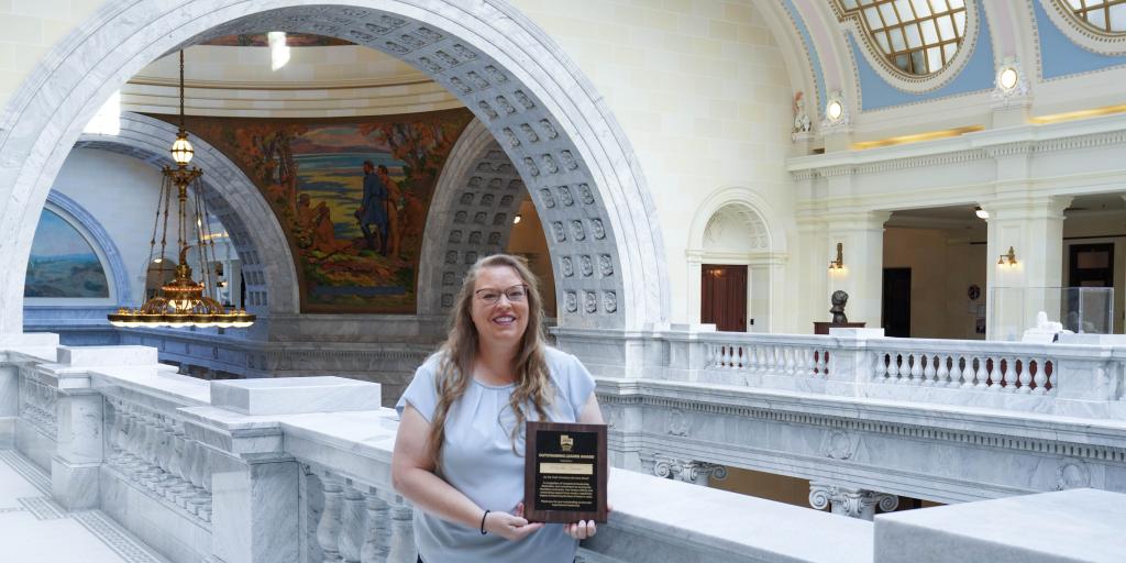 Jensen stands in the Utah State Capitol Building with her Outstanding Leader Award from the Utah Homeless Services Board