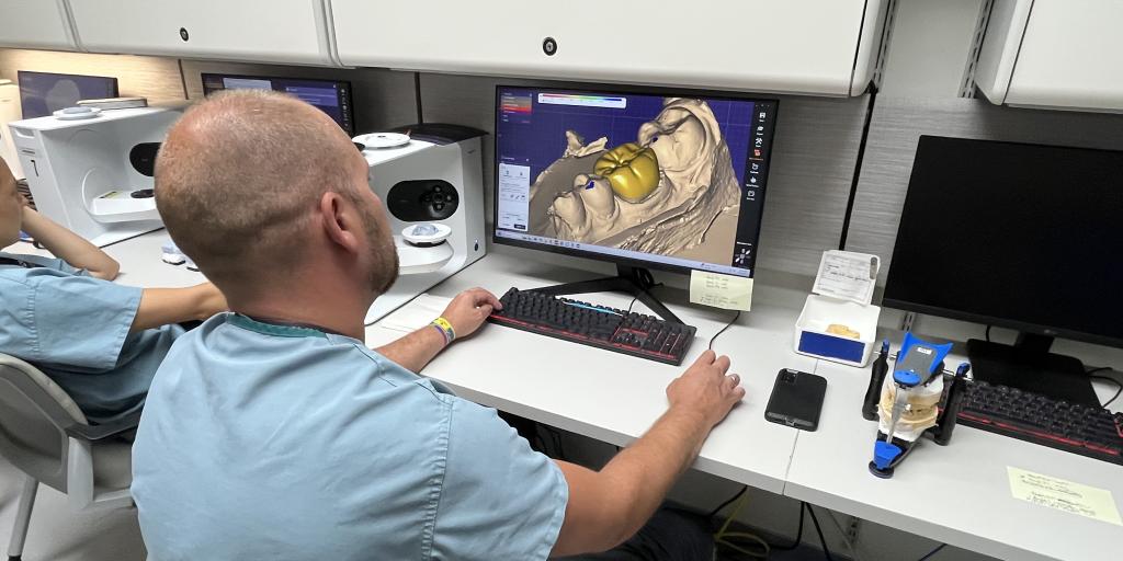 Man looking at computer screen that shows a crown for a set of teeth.