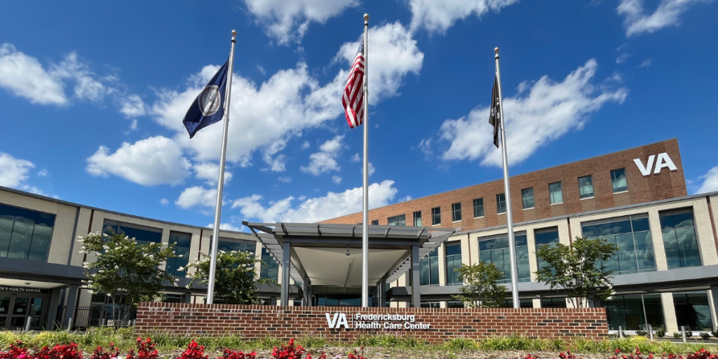 Veterans Affairs healthcare building is shown under a bright blue sky with scattered clouds. 