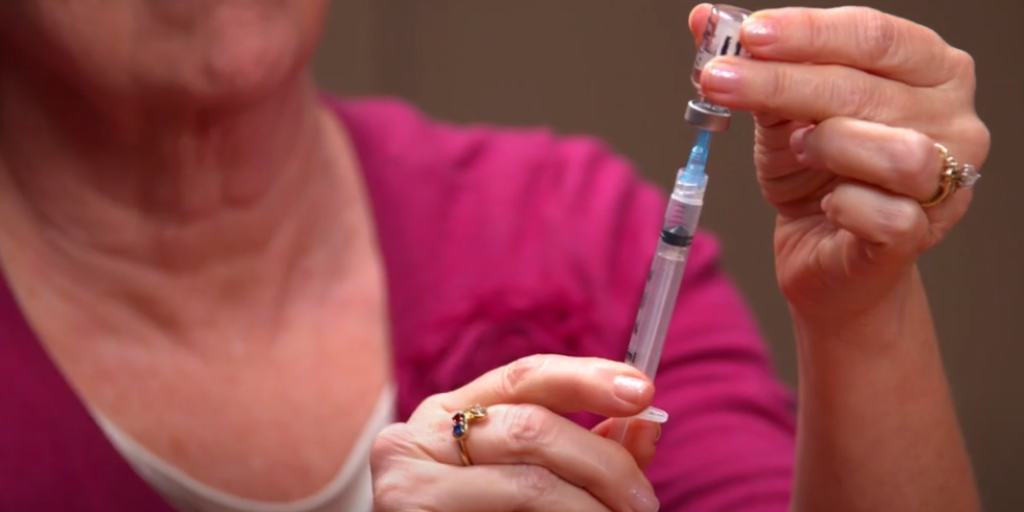 close up of woman's hands drawing medicine from a vial with a syringe