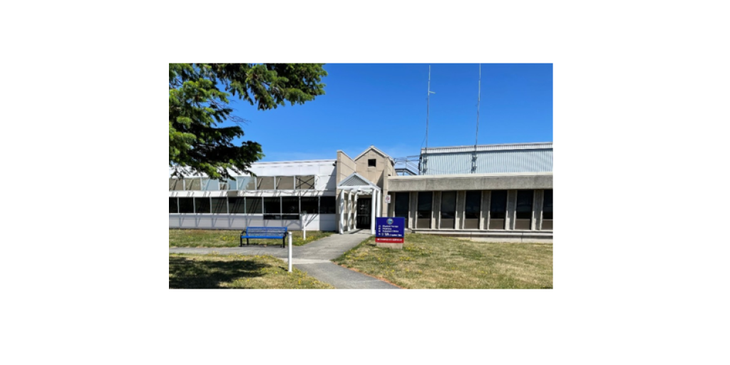 outdoors, clear blue sky,  building, grass, tree, bench in front of building next to sidewalk.