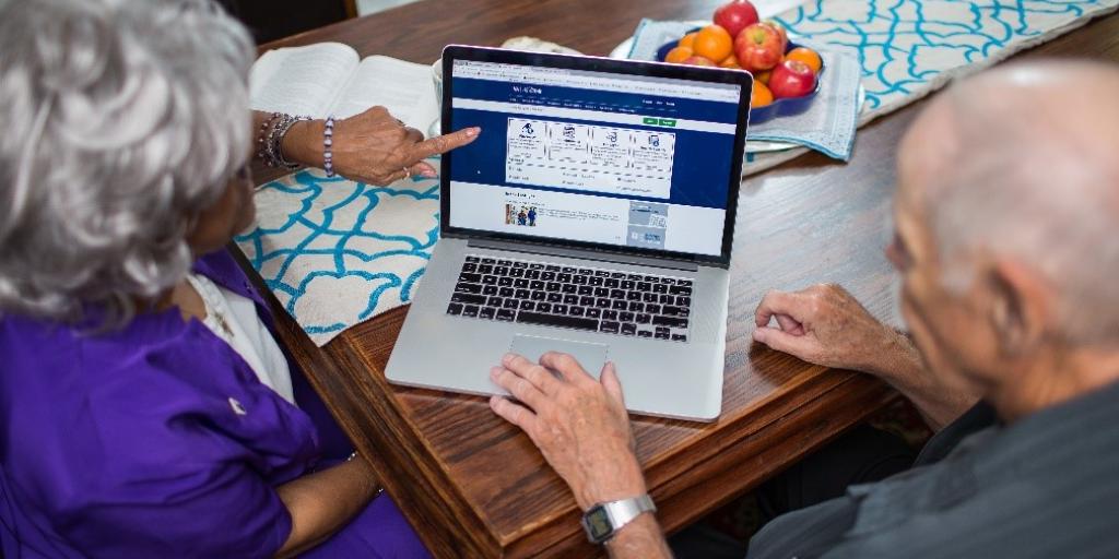 Older woman and man navigating an application on a laptop at a dining table