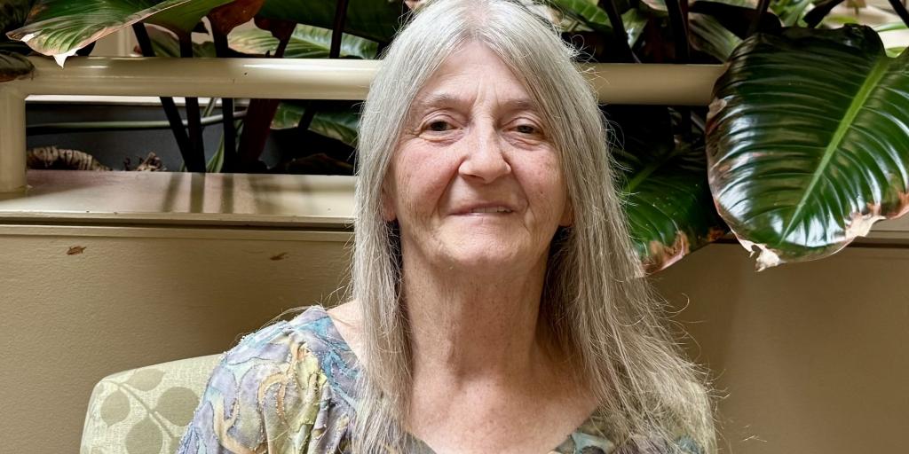 person sitting in front of plants and flags smiling