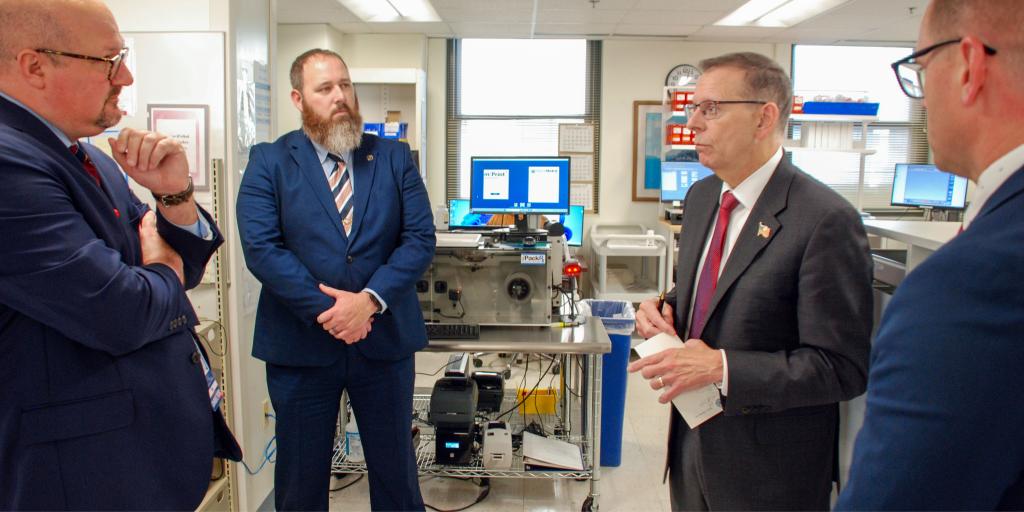 Men in suits standing in a pharmacy workspace.