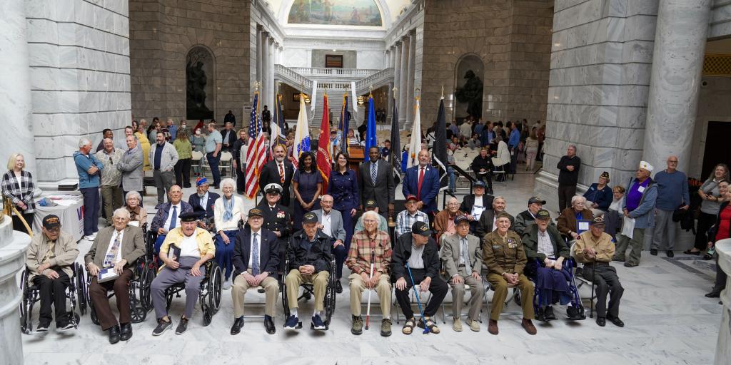 A groupf of 100-year-old Veterans sit in front of service flags after being honored by the state of Utah.
