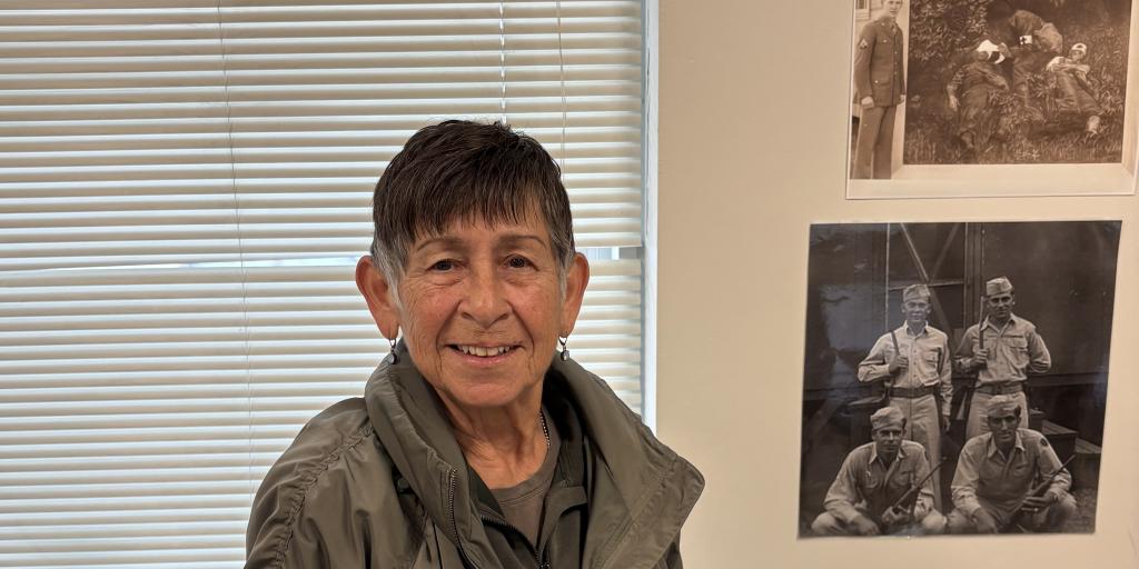 Woman facing cameras with old photos of soldiers behind her
