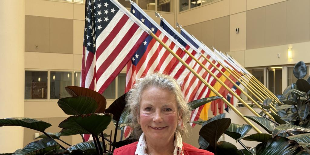 lady wearing a red vest standing in front of flags and plants