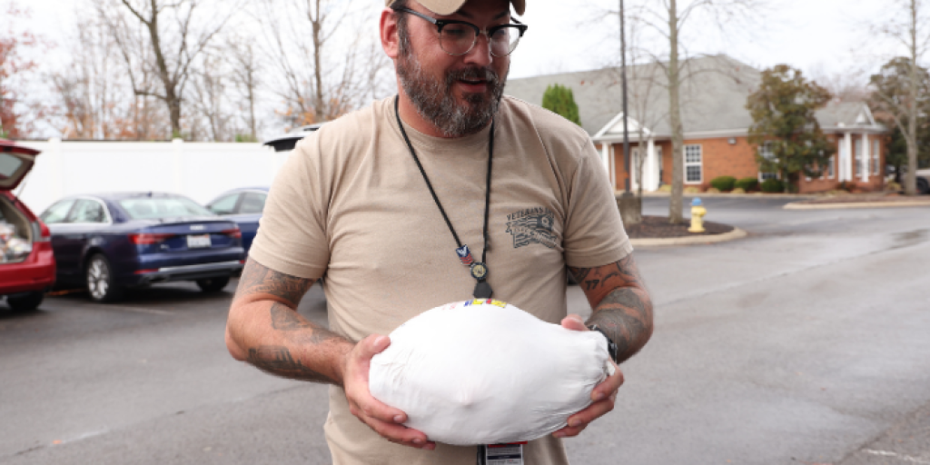 A man wearing a hat holds a Thanksgiving turkey.