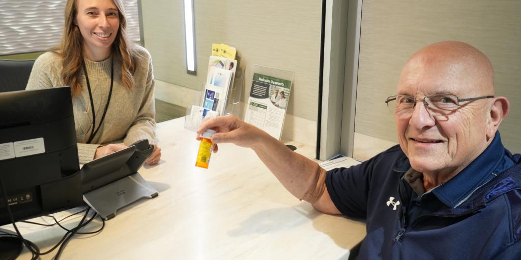 two people sitting at a desk - one holding a prescription bottle