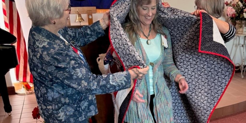 Mary Ogden being wrapped in the quilt by a representative of the Quilt of Valor organization.