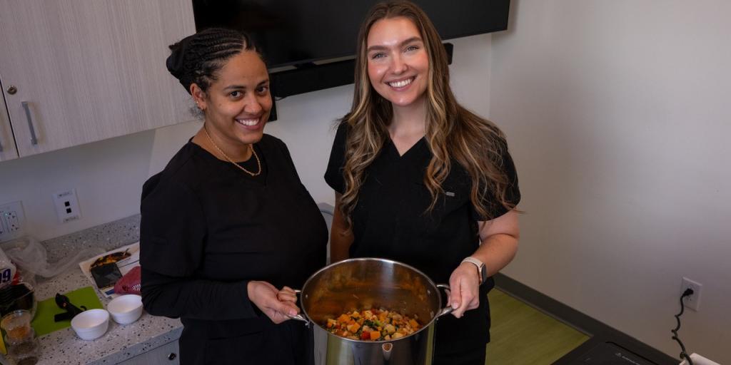 Two women in black shirts hold a pot of food.