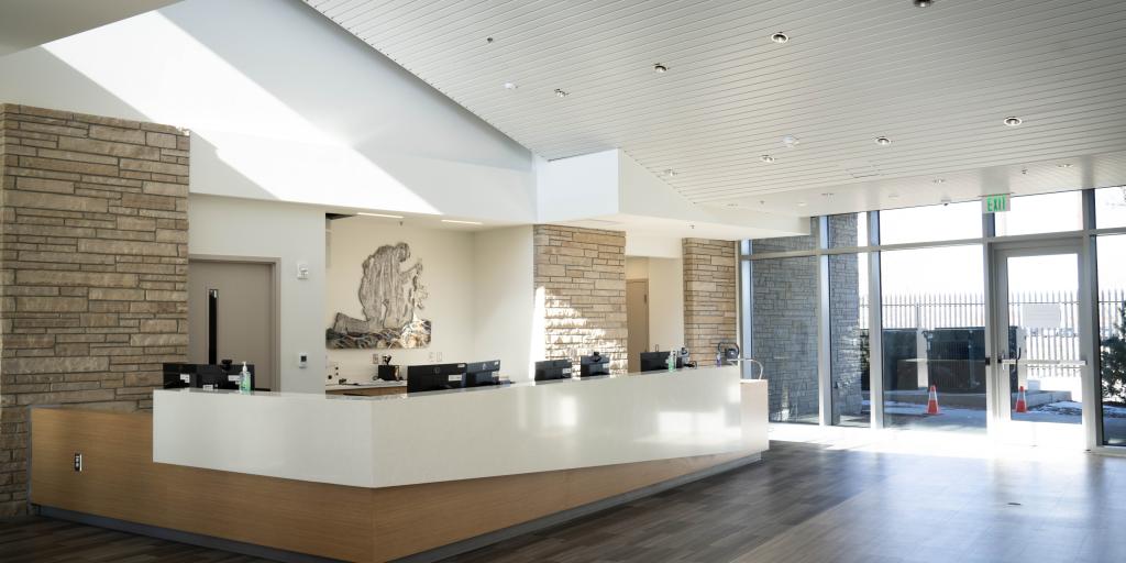Modern reception area with white desk, wooden floor, and large windows.