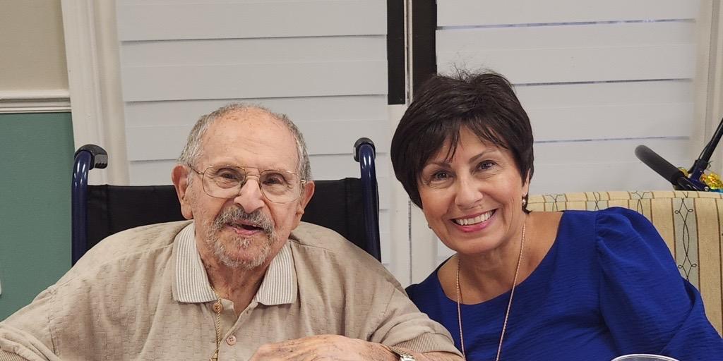 Elderly man and woman smiling at table with food and drinks.