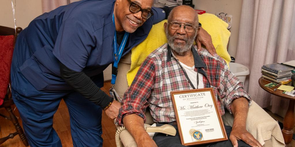 Home Based Primary Care Registered Nurse Antonio Clinkscales shares a joyful moment with 105‑year‑old World War II veteran Matthew E. Otey, whose service to the nation is honored through the compassionate care he now receives at home.