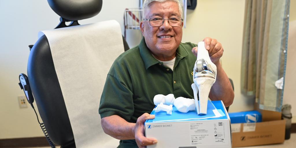 Man in green shirt holding a box and a model of a knee.