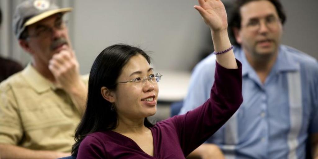 Woman with arm raised in a classroom full of people.
