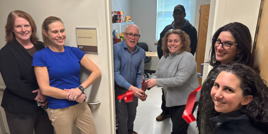 Group of six smiling people cutting a ribbon at an office opening.