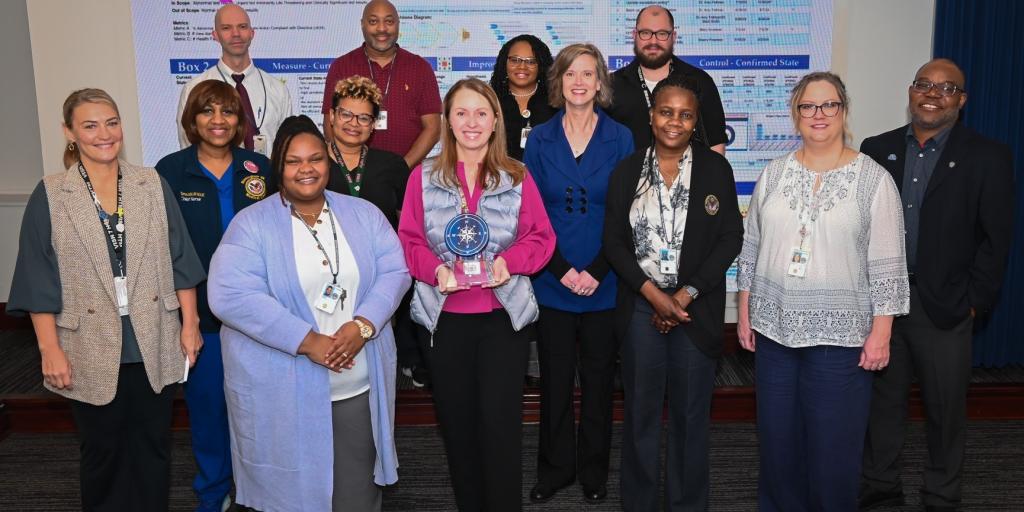 Group of 13 people standing together, one person holds an award.