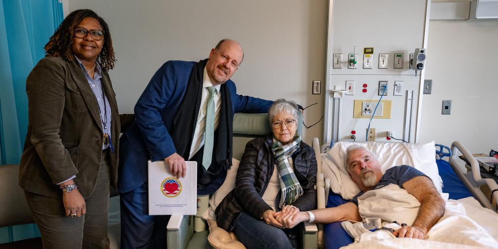Two women, a man, and a patient in a hospital bed.