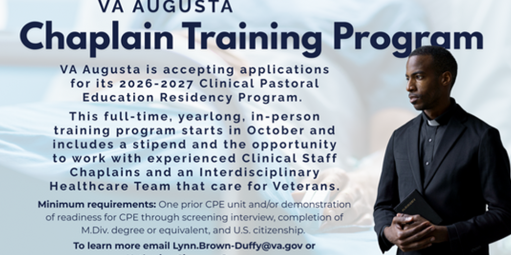 A man stands with his hands crossed in front of his chest, wearing a black suit and white shirt.