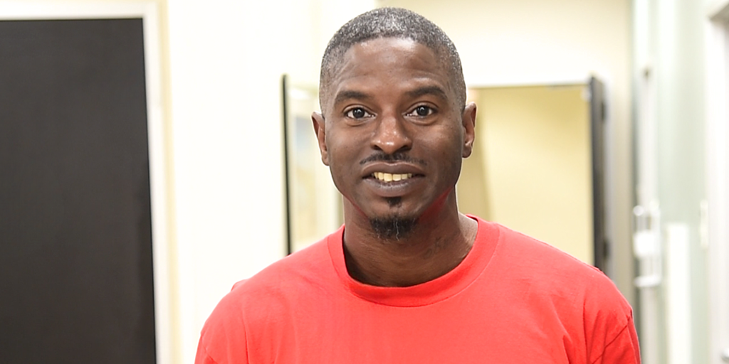 Man wearing a red shirt smiles in a hallway.