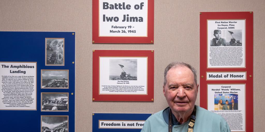 A man stands in front of a wall with historical posters and photos, smiling.