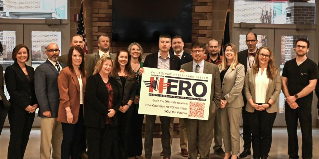 Group of people standing together holding a sign that says "HERO".