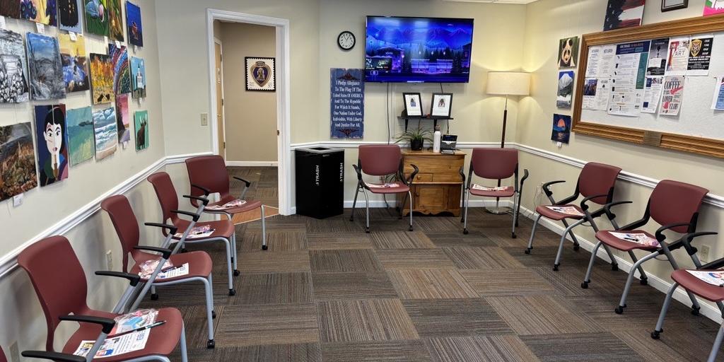 Waiting room with red chairs, artwork on walls, TV, and bulletin board.