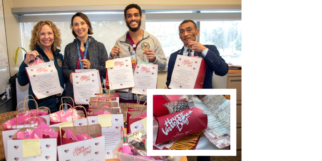 Four people holding signs stand behind a table of gift bags.