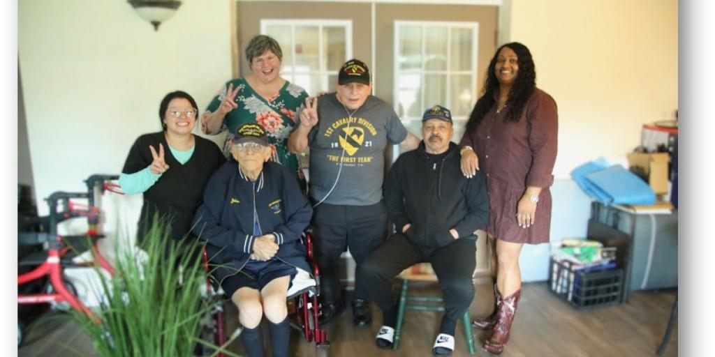 Group of veterans and caregivers posing for a photo in a living room.