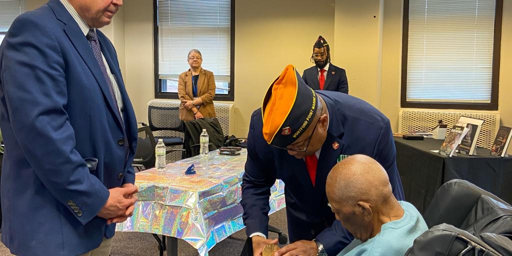 Two men in suits presenting a medal to a man seated man in a wheelchair. 