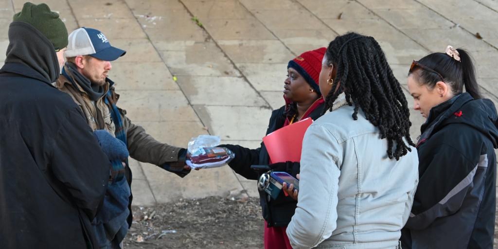 People gathered under a bridge, exchanging items and conversing.