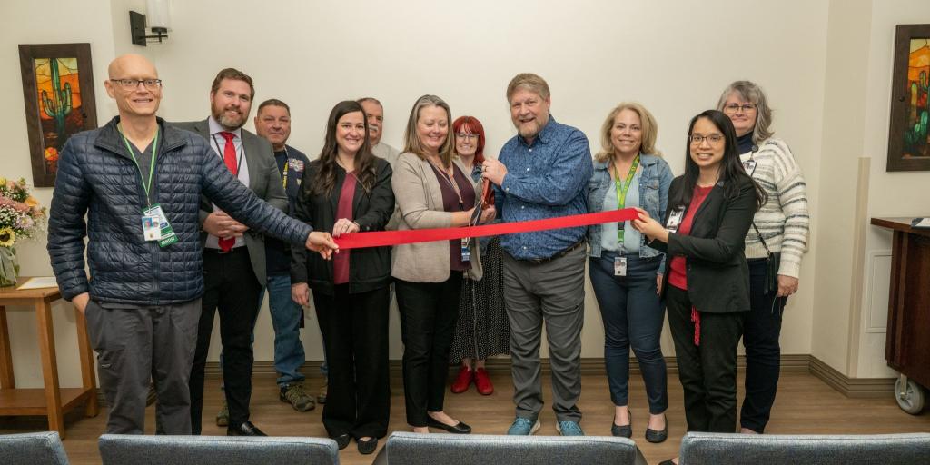 Group of people holding a red ribbon during a ribbon cutting ceremony.